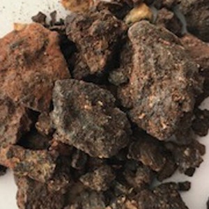 May include: A close-up of a pile of dark brown and reddish-brown resinous chunks. The resin is irregularly shaped and has a rough texture.