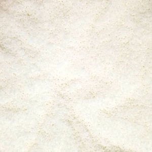 May include: A close-up view of a white granular substance filling a clear plastic bag. The bag is inside a brown cardboard box.