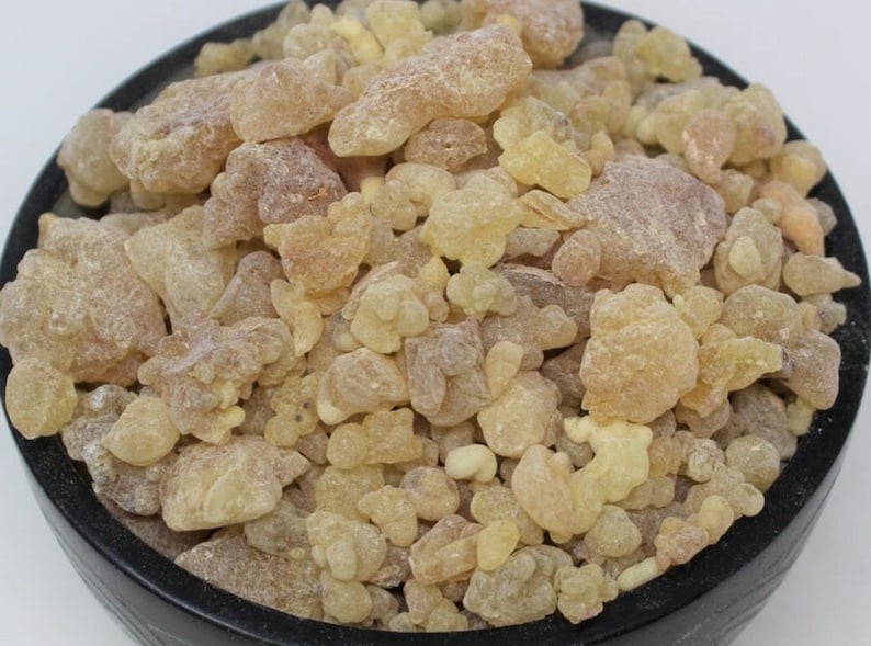 May include: A close-up view of a bowl filled with pale yellow and brown resin pieces. The resin is a natural ingredient used in incense and aromatherapy.