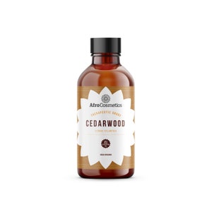 Puede incluir: Una botella de vidrio marrón con una tapa negra, etiquetada "AfroCosmetics Therapeutic Grade Cedarwood Cedrus Atlantica 100% Pure Essential Oil USDA Organic".
