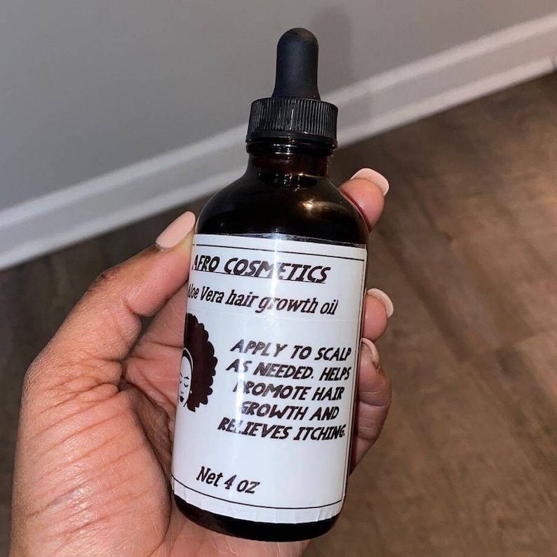 Puede incluir: Una botella de vidrio marr&oacute;n con un gotero negro y una etiqueta blanca que dice "AFRO COSMETICS Aloe Vera hair growth oil" y "APPLY TO SCALP AS NEEDED. HELPS PROMOTE HAIR GROWTH AND RELIEVES ITCHING Net 4 oz".
