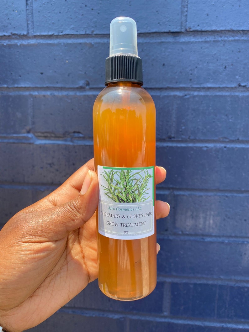 May include: A brown glass bottle with a black spray top and a white label. The label reads "Afro Cosmetics LLC Rosemary & Cloves Hair Grow Treatment 8oz".