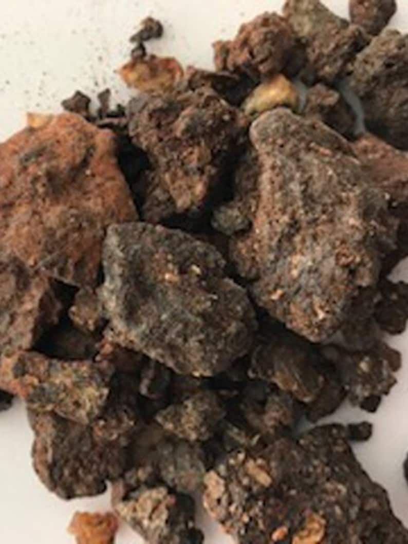 May include: A close-up of a pile of dark brown and reddish-brown resinous chunks. The resin is irregularly shaped and has a rough texture.
