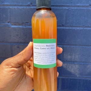 May include: A brown glass bottle with a green label that reads "Ingredients: Rosemary, Cloves, Castor oil, Water. Directions: Apply the hair grow treatment on the scalp and massage. Do not rinse out. For best results, use daily or 4 times a week. Recommended for all hair types. Shake well before use."
