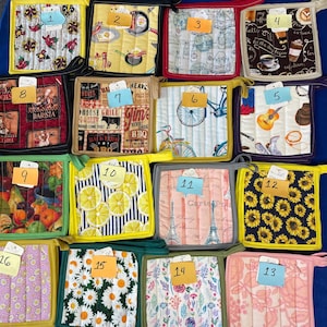 May include: A set of 16 colorful quilted pot holders with various designs, including lemons, sunflowers, bicycles, and coffee cups. Each pot holder has a yellow border and a number from 1 to 16.