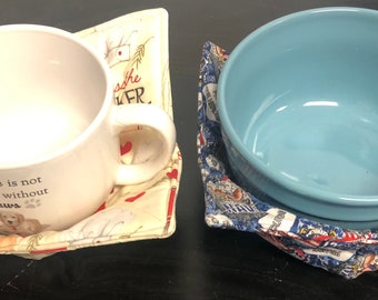 May include: Two fabric bowl and mug cozies. The mug cozy is cream with red hearts and the text "A house is not a home without paws". The bowl cozy is blue with a white and red pattern.