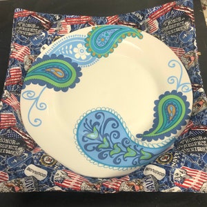May include: A white ceramic plate with a blue and green paisley design. The plate is sitting on a blue and red fabric with the words "Honor, Respect, Commitment" repeated on the fabric.