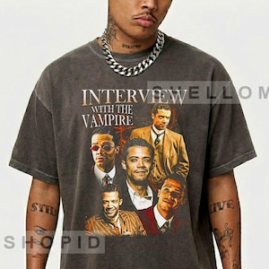 May include: Dark gray t-shirt featuring a graphic from "Interview with the Vampire." The design includes portraits of actors and the show's title in white and orange lettering. The shirt has a vintage, worn look.