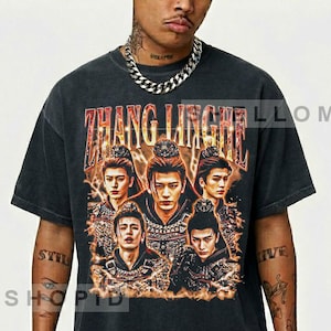 May include: A charcoal gray short-sleeve t-shirt featuring a graphic print of Zhang Linghe in multiple poses with fiery orange and yellow accents. The text ZHANG LINGHE is printed in a bold, distressed font above the central character portraits.