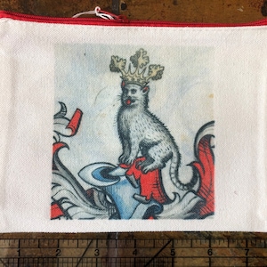Puede incluir: Bolsa de lona blanca con cremallera roja. La bolsa presenta una ilustración vintage de un gato coronado de pie sobre un escudo rojo y azul.