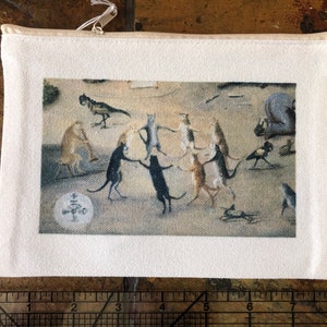 May include: A white canvas zippered pouch with a printed image of a group of cats dancing in a circle. The image is in a cartoon style with bright colors.
