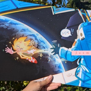 May include: A digital illustration of a yellow and orange cartoon character with a red and white shoe floating in space. The character is smiling and waving. A blue astronaut is reaching out to the character from a space station. The background is a dark blue space with a blue and green planet in the distance. The text "Jasmine By The Bay" is in the lower right corner of the image.