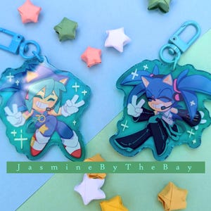 May include: Two blue and green character keychains with a blue and white star pattern. The keychains feature a blue and green character with a blue and white star pattern. The keychains are attached to a blue metal ring.