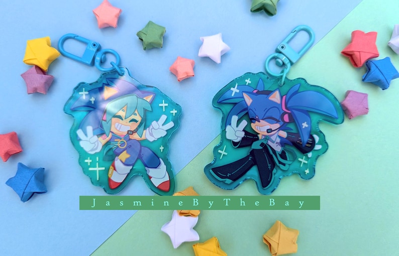 May include: Two blue and green character keychains with a blue and white star pattern. The keychains feature a blue and green character with a blue and white star pattern. The keychains are attached to a blue metal ring.