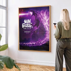 May include: A framed poster for the film "Shin Godzilla" in 4K, featuring a purple Godzilla illustration with a beam of light. The poster is in a wooden frame and mounted on a white wall.
