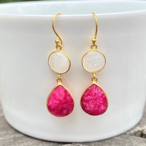 May include: Gold dangle earrings with a round white gemstone and a teardrop shaped pink gemstone.