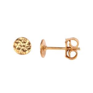 May include: A pair of gold hammered disc stud earrings. The earrings are small and round, with a textured surface. The earrings are made of 14k gold and are perfect for everyday wear.