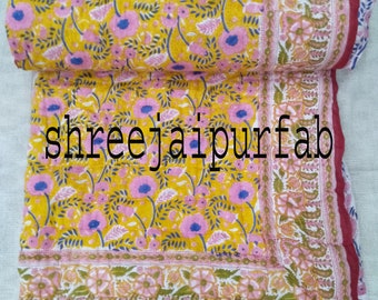 May include: A yellow and pink floral patterned quilt with a red border. The quilt is folded in half and has a text label that reads "shreejaipurfab".