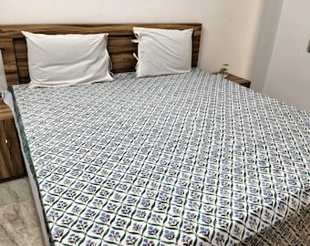 Puede incluir: Un cubrecama blanco con un patrón floral azul y verde. El cubrecama está en una cama con dos almohadas blancas.