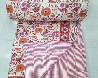 May include: A white cotton quilt with a floral print on one side and red and white stripes on the other side. The quilt is folded in half and the floral side is facing up.