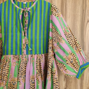 May include: A green and blue striped dress with a pink and green tiger print. The dress has a tie at the neck and a gathered skirt.