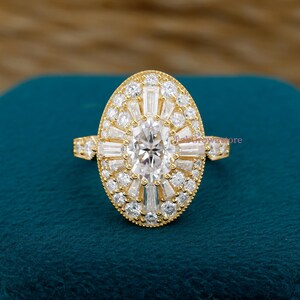 May include: A gold ring with a large oval-shaped center stone surrounded by smaller, sparkling stones. The ring features a halo design with a mix of round and baguette-cut stones, creating a dazzling effect. The band is also adorned with smaller stones.