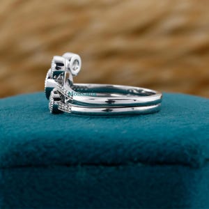 May include: A set of two silver rings with small, clear gemstones. The rings are stacked together, with one featuring a larger, rounded gemstone and the other a simple band. The word "Moissanita" is visible on the side of the ring. The rings are on a teal surface.