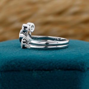 May include: A set of two silver rings, one with a curved design and small accent stones, the other a simple band. The rings are set against a teal background. The word "Moissanita" is visible on the side of the ring.