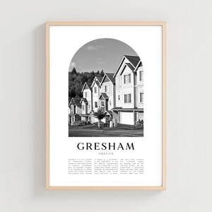 Può includere: Stampa incorniciata in bianco e nero con una fila di case sotto un arco, con il testo "Gresham Oregon" in basso. Le case hanno rivestimenti bianchi e tetti scuri. La stampa è in una cornice di legno chiaro.