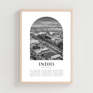 May include: Black and white framed print featuring an aerial view of Indio, California, under an arched design. The print includes the city's name and descriptive text at the bottom. The frame is a light wood color.