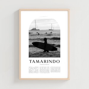 Può includere: Stampa incorniciata in bianco e nero con un surfista con una tavola da surf nell'oceano. Lo sfondo include barche e un cielo nuvoloso. La parola "Tamarindo" è stampata in basso, con "Costa Rica" sotto.