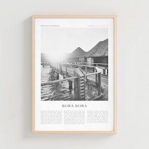 Könnte beinhalten: Gerahmter Schwarz-Weiß-Druck, der einen Holzsteg zeigt, der zu Gebäuden mit Strohdächern über Wasser führt. Der Druck trägt die Aufschrift "FRENCH POLYNESIA" und "BORA BORA". Das Bild ist in einem hellen Holzrahmen präsentiert.
