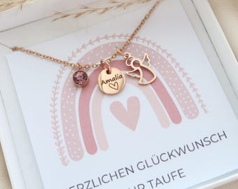 May include: A rose gold-toned necklace featuring a small round pink crystal charm, a circular pendant engraved with the name Amalia and a heart, and an angel-shaped charm, presented on a card with a rainbow and the text HERZLICHEN GLÜCKWUNSCH ZUR TAUFE.