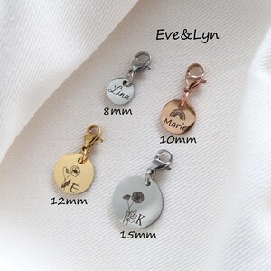 Op de afbeelding: Vier ronde metalen bedels met karabijnsluitingen in zilver-, goud- en ros&eacute;goudkleuren. De bedels zijn gegraveerd met namen, letters en bloem- of regenboogontwerpen. Labels geven maten van 8mm, 10mm, 12mm en 15mm aan. De tekst Eve&Lyn is zichtbaar.