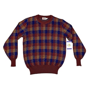 May include: A vintage sweater in a plaid pattern featuring shades of burgundy, blue, and tan. The sweater has a crew neck and long sleeves with ribbed cuffs. A tag is attached to the sleeve. The sweater is made of a soft, knitted material.