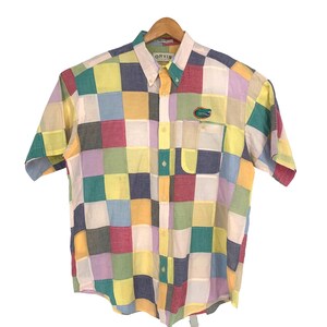 May include: A short-sleeved button-down shirt with a patchwork design in various colors, including yellow, red, blue, and green. The shirt has a chest pocket and a small embroidered logo. The brand name "ORVIS" is visible on the collar.