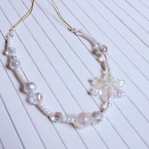 May include: A necklace with a snowflake pendant, crafted from small white beads, iridescent beads, and clear crystal beads. The snowflake pendant has an iridescent finish. The necklace is displayed on a white surface.