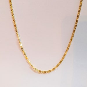 Puede incluir: Un collar de cadena de oro con un diseño delicado y texturizado. La cadena está hecha de pequeñas formas ovaladas enlazadas.