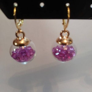 May include: A pair of gold hoop earrings with a clear glass orb filled with small pink crystals.
