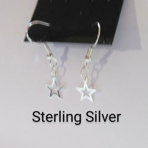 Puede incluir: Un par de pendientes de estrella de plata de ley con un diseño sencillo. Los pendientes están sobre un fondo negro.