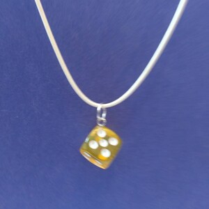 May include: A silver chain necklace with a yellow dice pendant. The dice has white dots on each side.