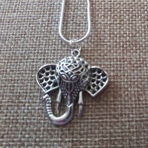 Op de afbeelding: Een zilveren ketting met een sierlijke olifant hanger. De olifant is versierd met ingewikkelde patronen en heeft een opgetrokken slurf.