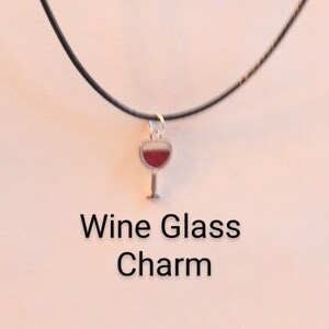 Puede incluir: Un dije de copa de vino de plata en un collar de cordón negro. El dije está relleno de esmalte rojo para parecerse al vino.
