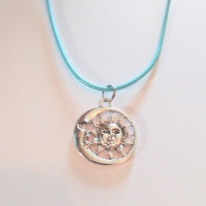 May include: A silver necklace with a sun and moon pendant on a light blue cord.