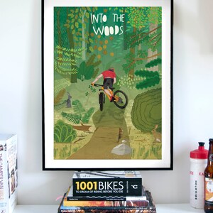 Peut inclure: Une affiche encadr&eacute;e avec une illustration color&eacute;e d'une personne faisant du v&eacute;lo de montagne dans une for&ecirc;t. L'affiche porte le texte "Into the Woods" en haut.