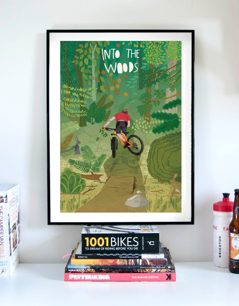 Peut inclure: Une affiche encadr&eacute;e avec une illustration color&eacute;e d'une personne faisant du v&eacute;lo de montagne dans une for&ecirc;t. L'affiche porte le texte "Into the Woods" en haut.