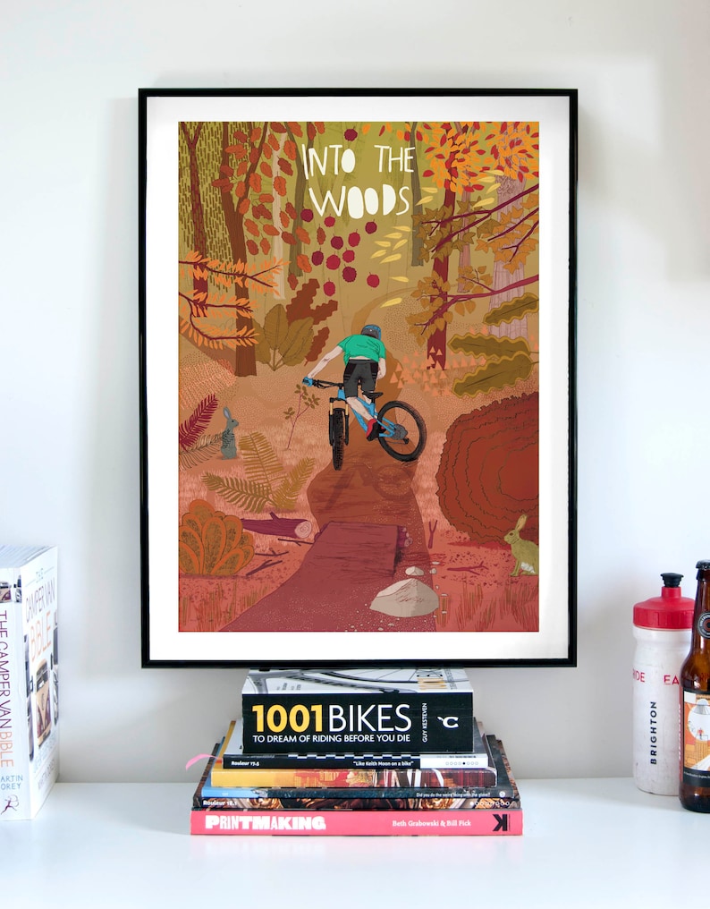 Peut inclure: Une illustration color&eacute;e d'un cycliste de montagne traversant une for&ecirc;t. Le texte "INTO THE WOODS" est en haut de l'image.