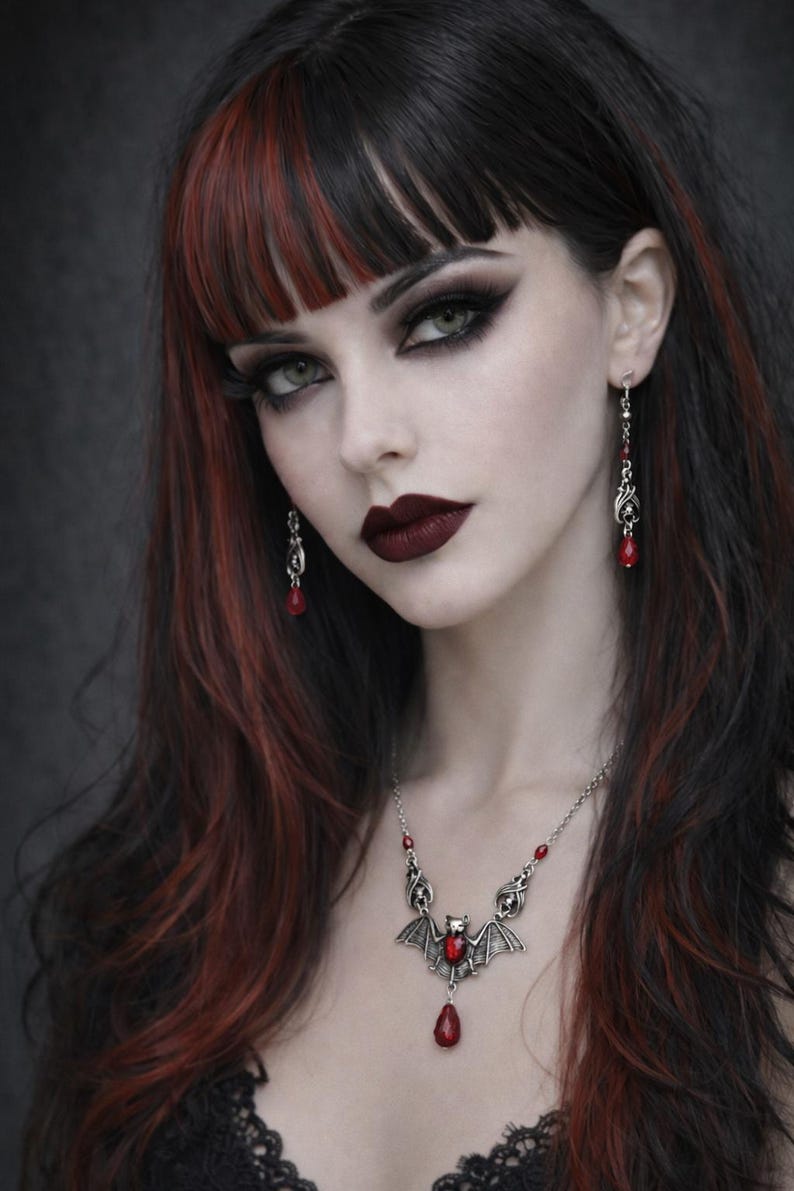 May include: A woman with dark hair, red highlights, and dark makeup. She wears a silver necklace with a bat pendant and red gemstone, matching earrings, and dark lipstick. The overall aesthetic is gothic.