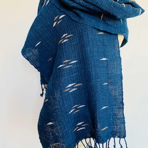 Peut inclure: Écharpe tissée bleu foncé avec des accents blancs et bronzés. L'écharpe est drapée sur un mannequin et présente une bordure à franges. Le tissu a un aspect texturé et un motif de petits tirets horizontaux.