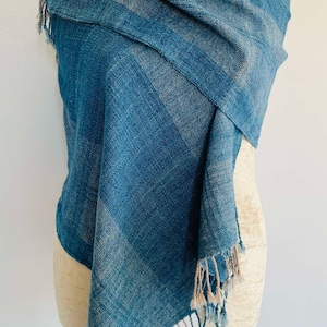 May include: A blue and white handwoven cotton scarf with fringe. The scarf is draped over a white mannequin.
